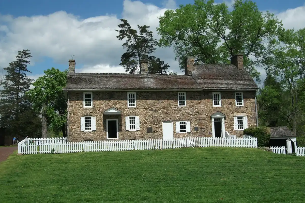 Stone farmhouse with a white fence and a wide lawn