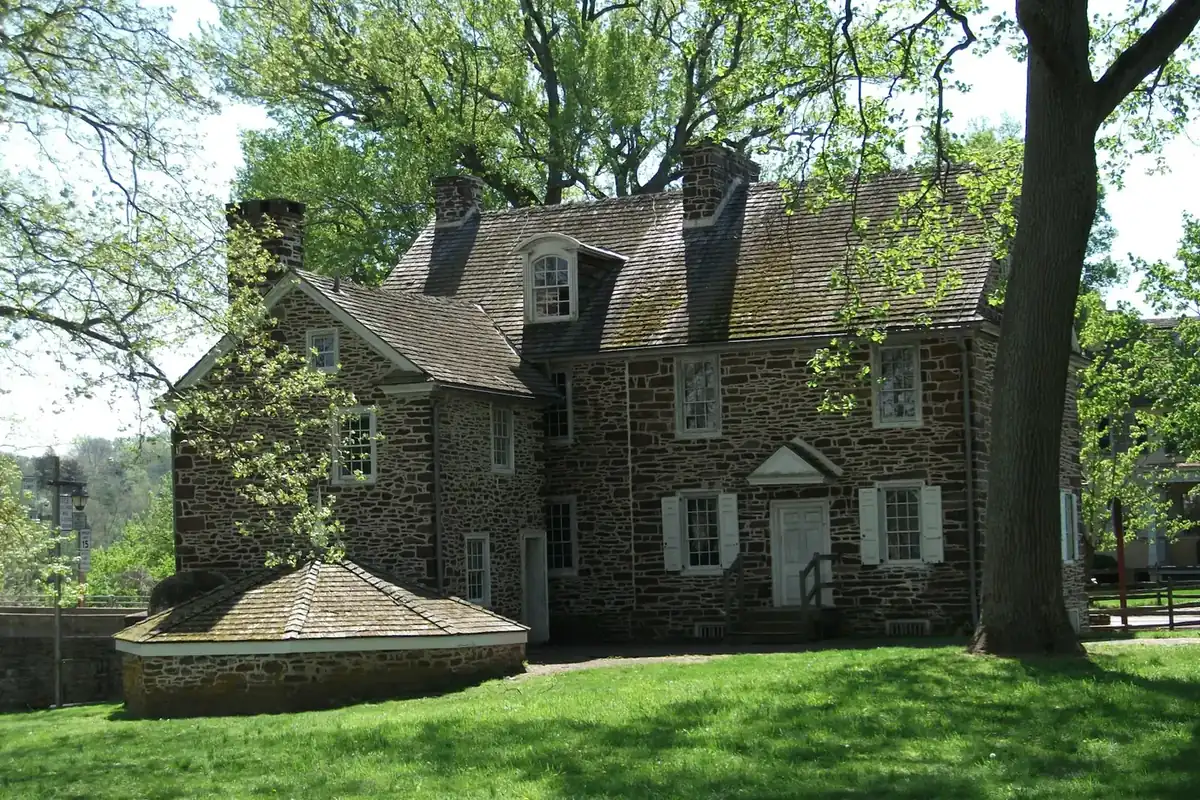 Older stone house with dark shutters under large shade trees