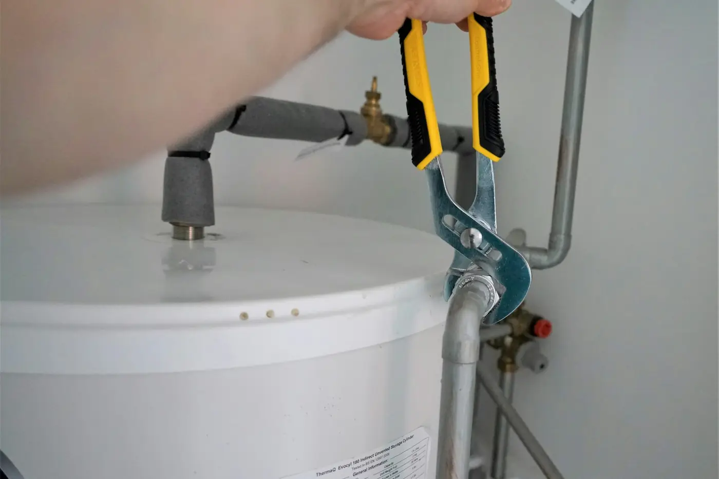 Plumber tightening a water line fitting on top of a tank water heater