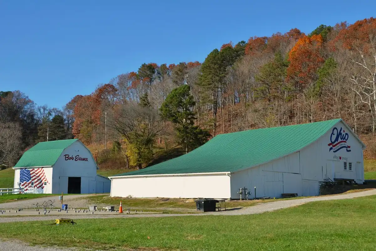 White barns with green roofs below hills of fall color